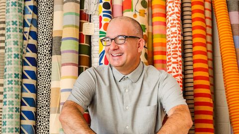 Vince Bravo sits in front of large rolls of colorful patterned textiles by Alexander Girard.