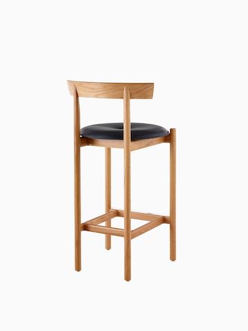 An oak Comma Stool with a seat pad, viewed from the back at an angle.
