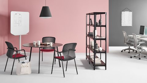 Three Keyn side chairs in black with crimson seats surround a round table in a small dining area in a larger workplace.