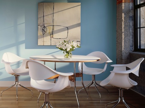 Four white Nelson Swag Leg Armchairs surround a round Nelson Swag Leg Table.