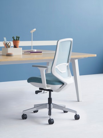 A grey POSH Express 2 Chair with a white frame and blue textile seat next to an Optimis Desk in a workstation setting.
