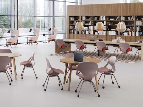 Two round tables each with four light brown Zeph Side Chairs in front of a long rectangular project table with eight light brown Zeph Side Chairs with light brown knit covers in a common area