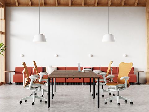 Four Mirra 2 chairs in ochre surround an OE1 table in the middle of a collaborative space with a Chadwick sofa in the back.