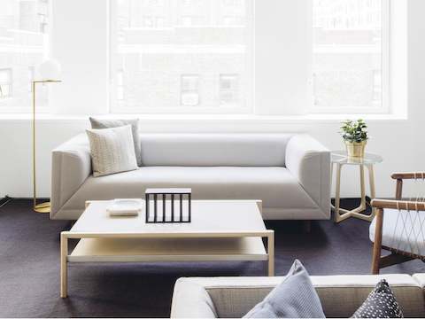 A residential setting featuring a light gray Rolled Arm Sofa with two pillows next to a glass-top end table.