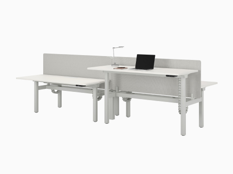 A four desk configuration of Nevi Sit-to-Stand Desks in white with gray fabric screens. Front right desk raised to standing height.