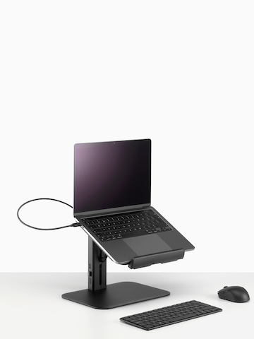 A black Lana laptop stand with laptop, keyboard and mouse viewed from a side angle.