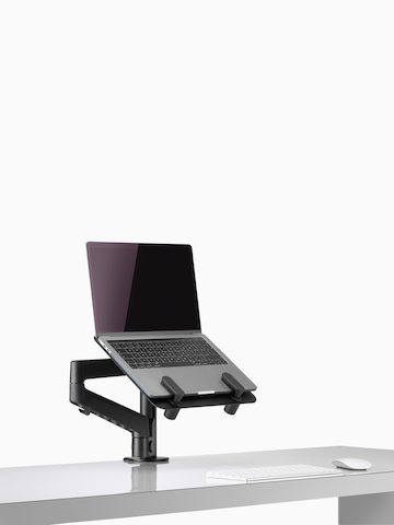 Side angle view of an open laptop raised from a desk and supported by a black Lima Laptop Mount and Lima Monitor Arm. Select to go to the Lima Laptop Mount product page.